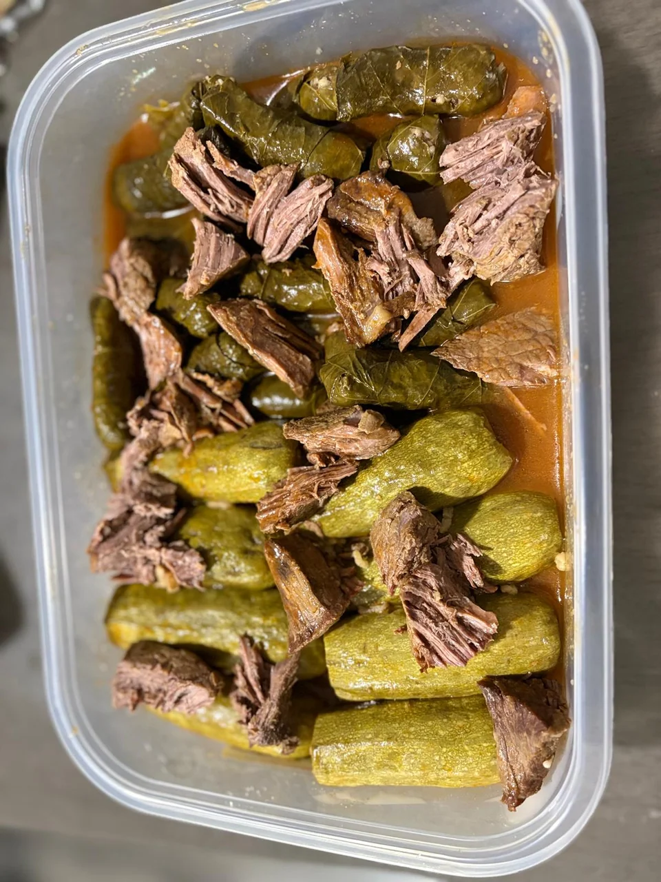 A foil tray of stuffed zucchini, grape leaves and pieces of meat.