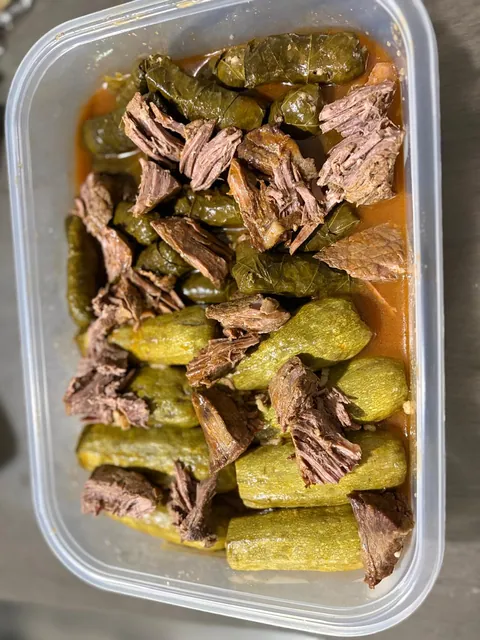 A foil tray of stuffed zucchini, grape leaves and pieces of meat.