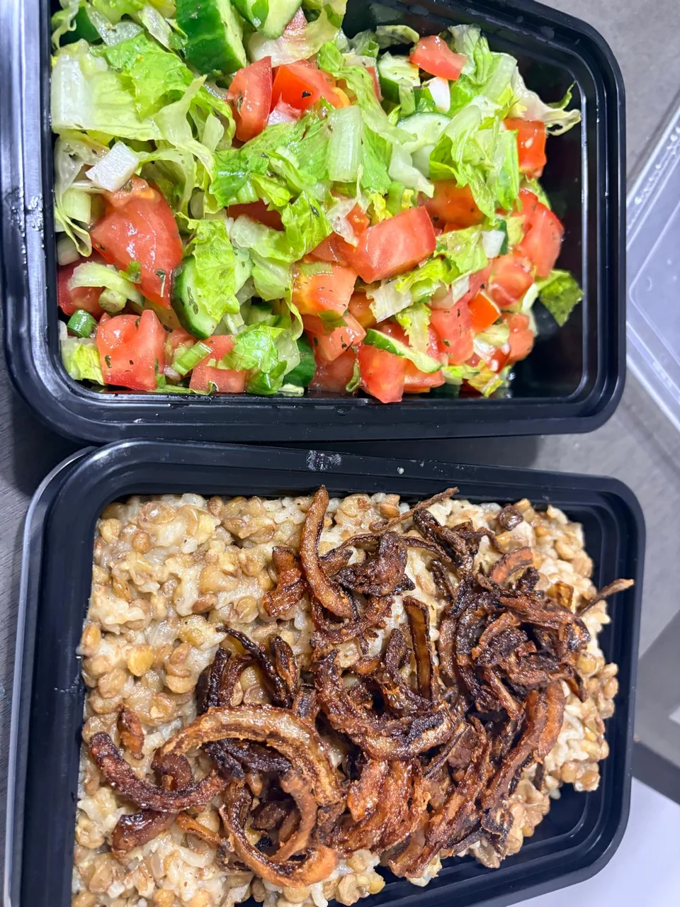 Individual containers of fresh salad and rice with lentils and browned onions.