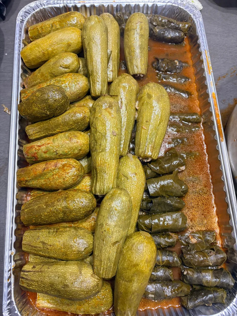 Neatly arranged stuffed zucchini and grape leaves in a foil tray.