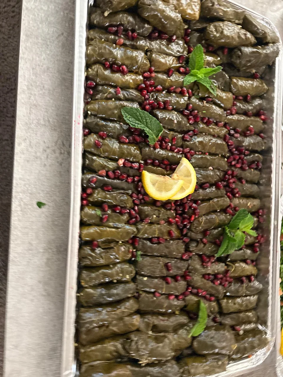 A long foil tray of grape leaves finished with lemon and pomegranate.