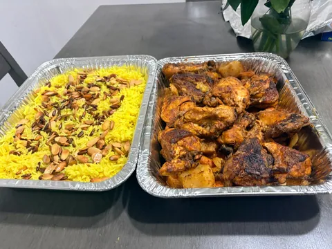 A tray of golden rice beside a tray of roasted chicken.
