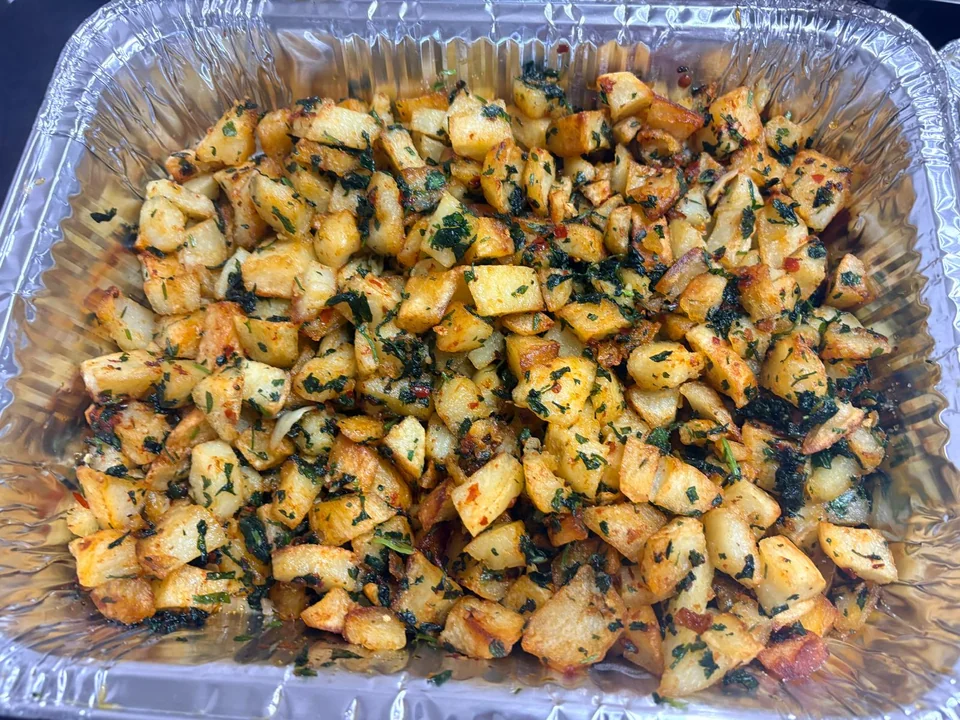 A foil tray of diced potatoes tossed with chopped herbs.