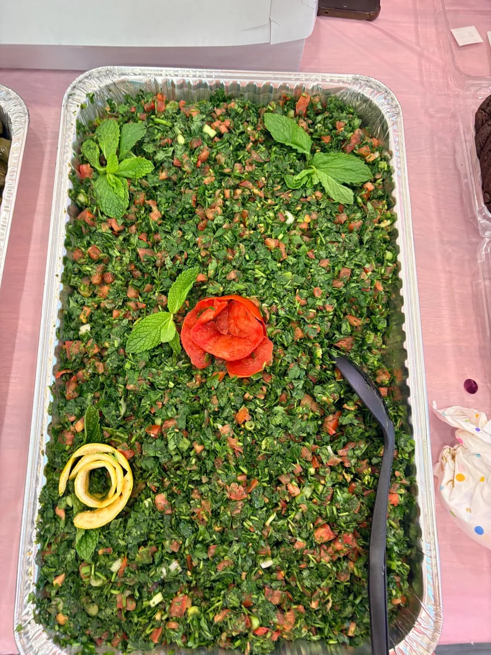A colorful tabbouleh tray with tomato, parsley and a rose-shaped garnish.