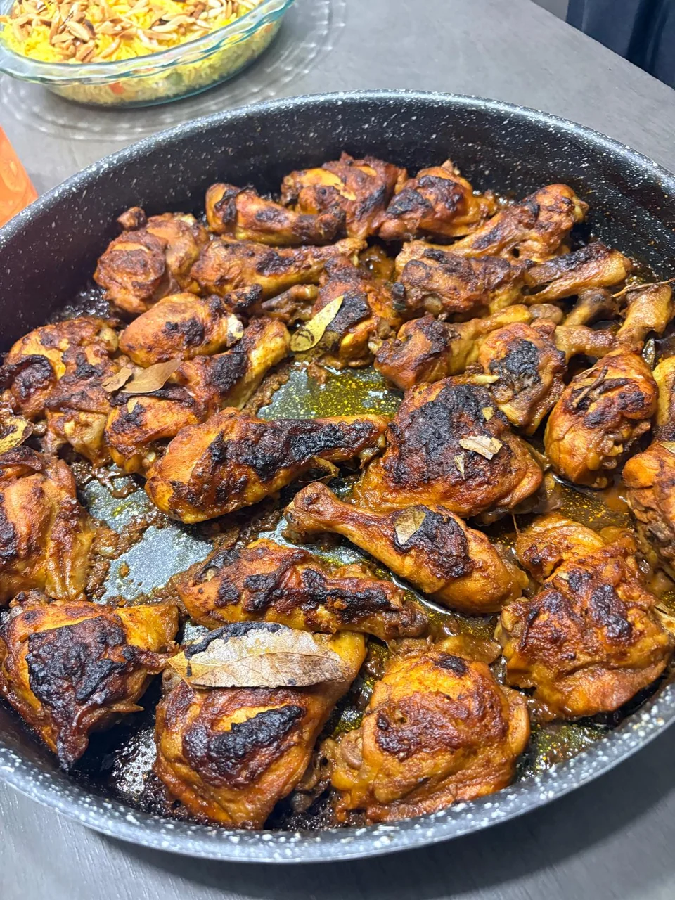 A foil tray of browned roasted chicken pieces with herbs.