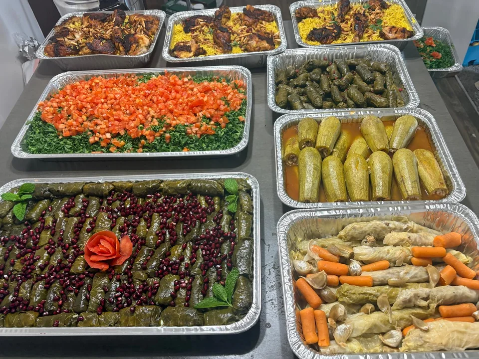 A table of rice, salad, grape leaves and stuffed vegetable trays.