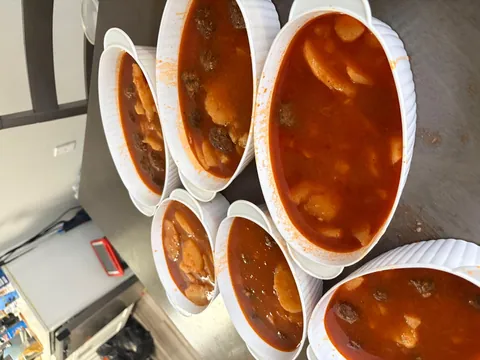 Several white bowls filled with a red stew and vegetables.