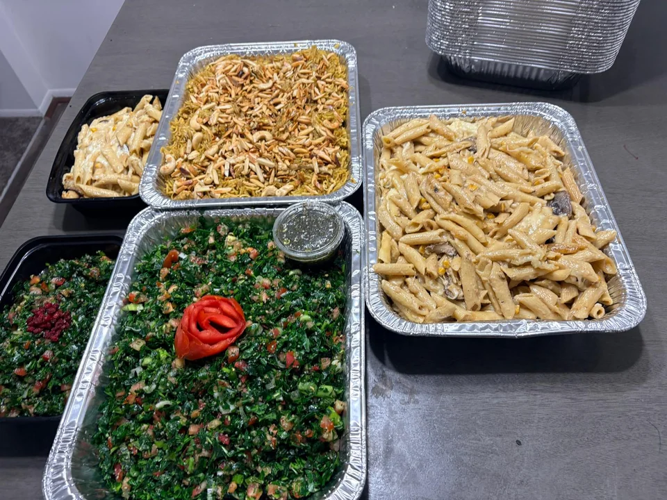 Family trays of rice, pasta and tabbouleh arranged on a table.