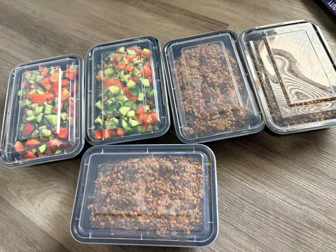 Prepared family trays with fresh salads and rice dishes, some with lids.