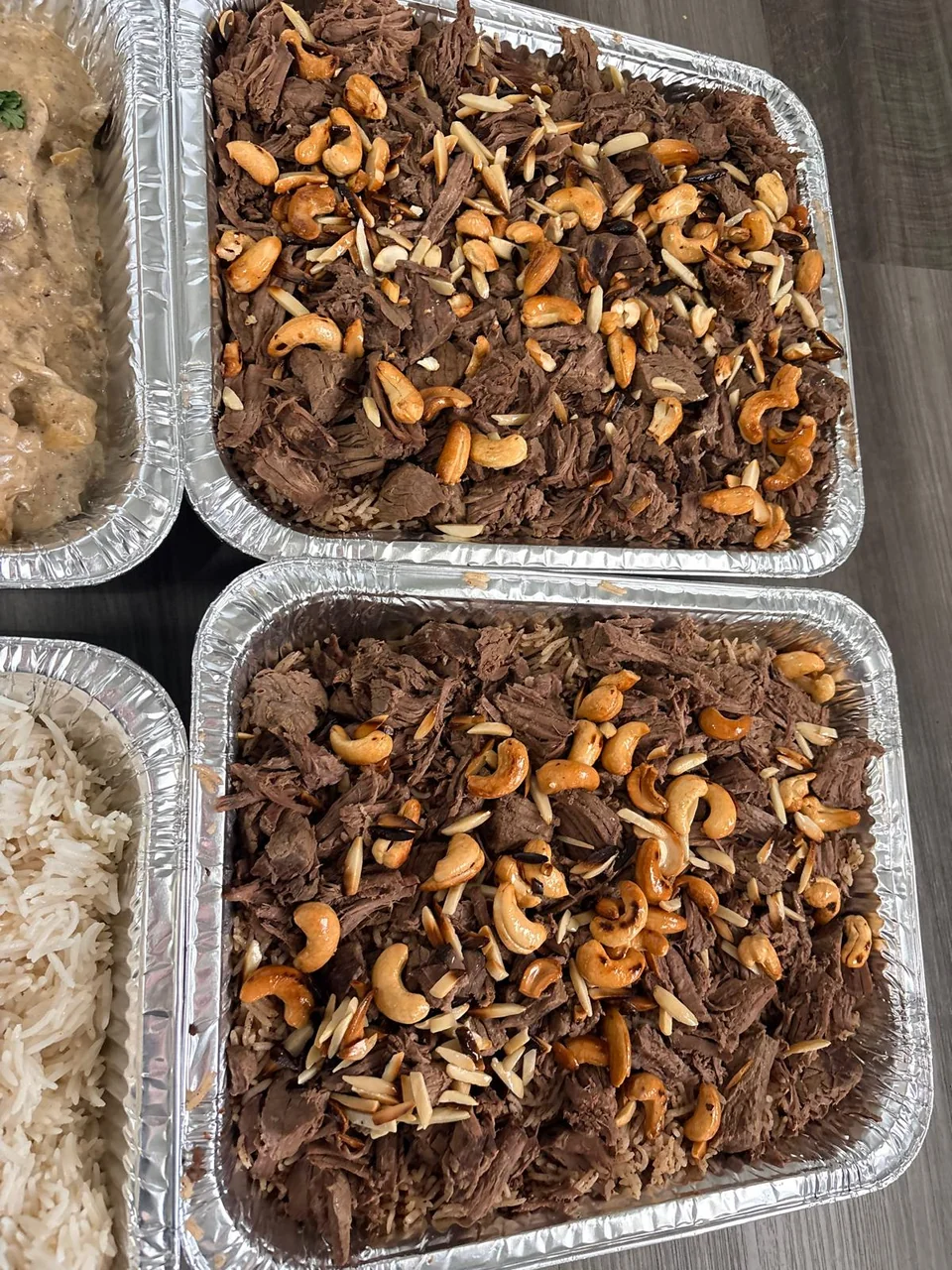 Two rice trays topped with meat and toasted nuts.
