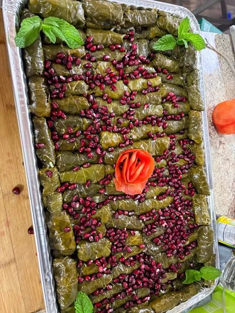 A tray of neatly rolled grape leaves with fresh mint, pomegranate and a tomato rose.